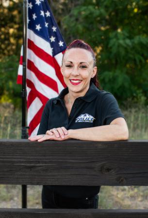 Krystal DeVoile leaning on a wooden fence standing in front of an American flag.